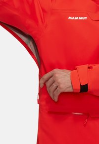 Rote wasserdichte Jacke mit einer Reißverschlusstasche, verstellbaren Bündchen und Logoplatzierung. Glatte Textur und praktisches Design für den Außeneinsatz.