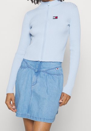 Vaaleansininen ribbattu vetskaritakki pitkähihaisilla hihoilla ja korkealla kauluksella, yhdistettynä farkkuhameeseen, jossa on joustava vyötärö ja taskut.