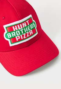 Červená baseballová čiapka s výrazným vyšívaným štítkom s textom "HUNT BROTHERS PIZZA" v bielej a zelenej farbe, umiestnená na štruktúrovanej prednej časti.