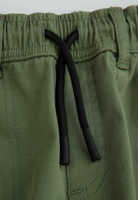 Zielone bawełniane szorty z elastycznym paskiem, wyposażone w czarny sznurek i gładką teksturę, z widocznymi szwami.