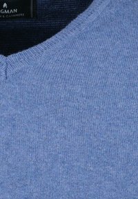 Hellblauer, gestrickter Pullover mit V-Ausschnitt. Weiche Textur und leicht gerippte Oberfläche. Etikett sichtbar in dunklem Stoff an der Oberseite.