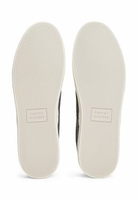 Sola di sneakers nere in tela con suola esterna in gomma grigia texturizzata. Presenta una suola intermedia bianca con il logo "TOMMY HILFIGER" in rilievo.