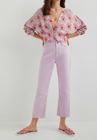 Cardigan à motifs floraux tricoté dans des tons roses et jaunes, associé à un jean droit violet clair et des tongs roses.