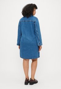 Denims kleita vidēji zila krāsā, līdz ceļgaliem, ar garām piedurknēm un taisnu piegriezumu. Pretrunīga šuvumu krāsa un noapaļota apakšmala.