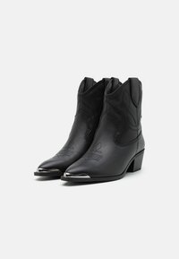 Zwarte leren cowboylaarzen met puntige neuzen, ingewikkelde stiksels en een metalen accent op de neus. Met hak ontworpen, met een gestructureerd oppervlak.