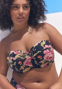 Mustast kangast lillemustriga bandeau bikiinide ülaosa, millel on suured roosad roosid ja rohelised lehed, kortsus kangadetail ja sile tekstuur.