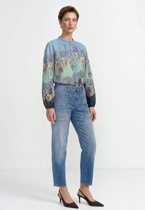 Woman wearing a blue floral button-up blouse, light blue high-waisted jeans with front pockets, and dark brown high-heeled shoes.