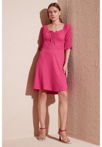 Pink ribbed dress with short puff sleeves, square neckline, and central tie detail. Paired with multicolored strappy heels.