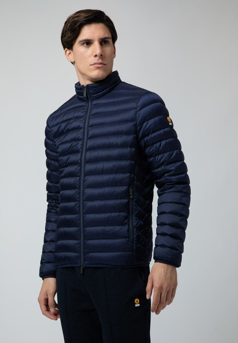 Giacca puffer blu navy con colletto alto, tasche con zip e taglio aderente. Presenta cuciture orizzontali testurizzate per l'isolamento.