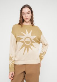 Πλεκτό πουλόβερ με σχέδιο σε μπεζ και ελιά χρώματα, διακοσμημένο με μοτίβα ηλιαχτίδας. Ολοκληρώνεται με στρογγυλή λαιμόκοψη και ριμπ μανσέτες.