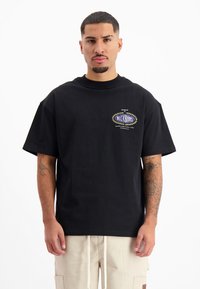 Zwarte katoenen T-shirt met korte mouwen, een ronde hals en een vooropdruk in blauw en goud. Draag het met lichtgekleurde cargobroek.