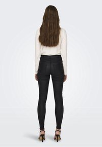 Černé skinny džíny s vysokým pasem a hladkým povrchem, kombinované s bílým dlouhým rukávem a černými vysokými podpatky.
