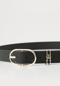 Ceinture en cuir noir avec une boucle ovale dorée et un accent doré mettant en avant des lettres entrelacées. Texture lisse et plusieurs trous d'ajustement.