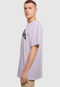 Lys lavendel bomulds T-shirt med korte ærmer, rund halsudskæring og fed sort trykt tekst. Glat tekstur og afslappet pasform.