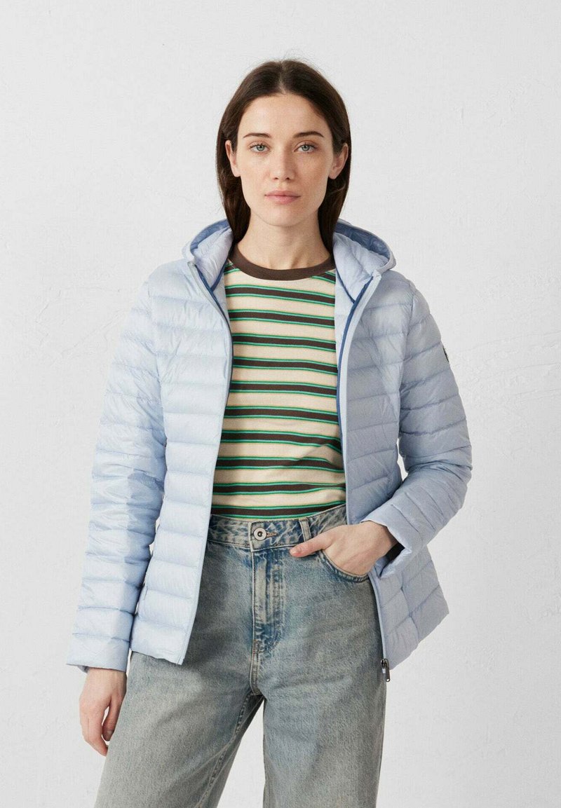 Lichtblauwe donsjas met capuchon, voorzien van een doorgestikt ontwerp. Draagt over een gestreept shirt met lange mouwen en een hoog uitgesneden spijkerbroek.