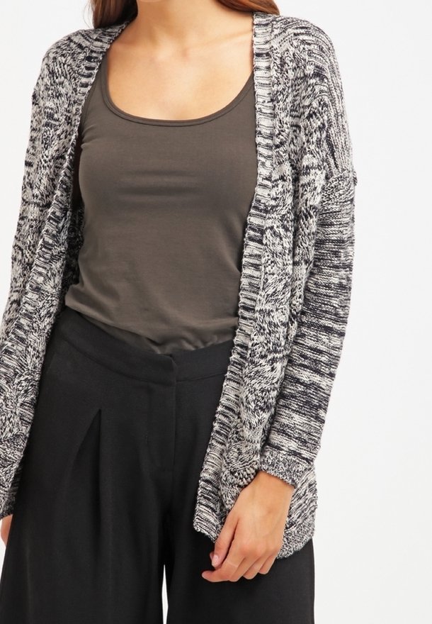 Cardigan ouvert en tricot marbré noir et blanc. Comprend des manches longues, des poignets côtelés et une coupe décontractée. Associé à un débardeur sombre et un pantalon taille haute.