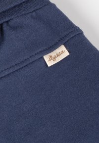 Dunkelblaues Baumwollgewebe mit glatter Textur, versehen mit einem genähten Saum und einem kleinen beigen Etikett mit dem Namen "stikkid."