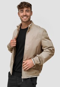 Bomber jacket beige con una textura suave, cuello y puños a rayas en contraste, detalle de logo bordado y cierre con cremallera.