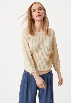 Maglione lavorato a maglia beige chiaro con strisce verticali, con un'ampia scollatura a barca e maniche a tre quarti, abbinato a pantaloni larghi blu scuro.