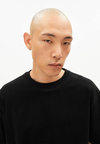 Zwart katoenen T-shirt met een geribbelde ronde hals, korte mouwen en een relaxte pasvorm. Close-up van een persoon die het draagt.