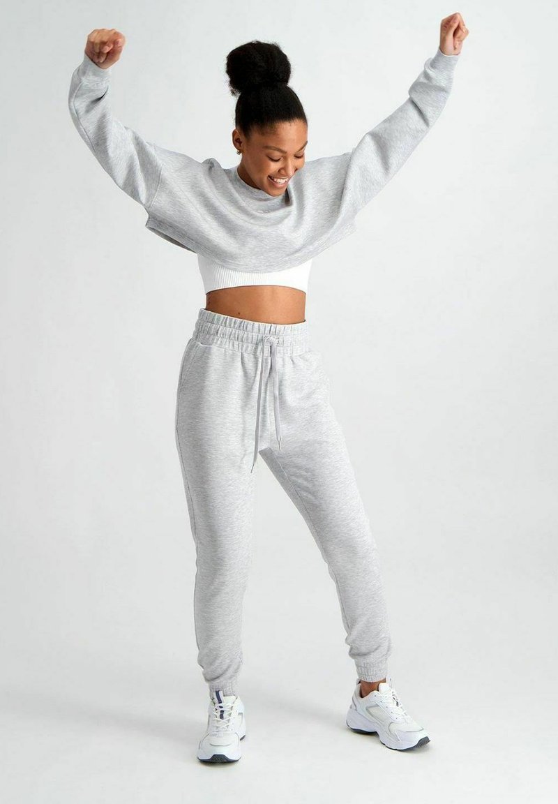 Lichtgrijze oversized sweatshirt met brede mouwen, gecombineerd met bijpassende joggers met een elastische tailleband. Witte sneakers maken de look compleet.