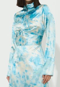 Abito a maniche lunghe in morbido e elasticizzato. Motivo tie-dye blu e crema con dettagli incrociati sul davanti e design a collo alto.