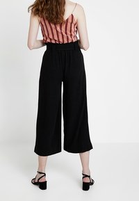 Black wide-leg pants with a high waist, featuring a textured fabric and pleated front, paired with a striped red and orange top.