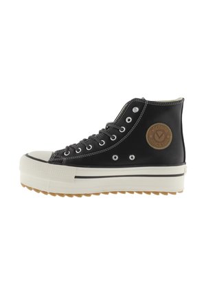 Sneaker alta nera con suola in gomma bianca, punta bianca e patch circolare marrone sul lato con la scritta "Victoria Since 1915."