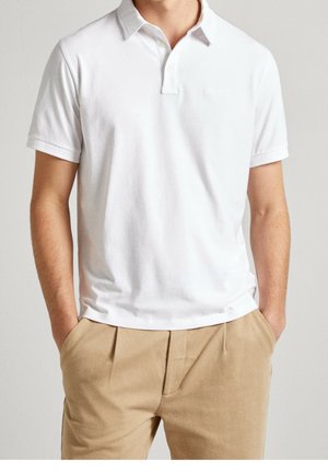 Polo shirt en coton blanc à manches courtes, avec un col et un petit logo brodé sur la poitrine, assorti à un pantalon beige.