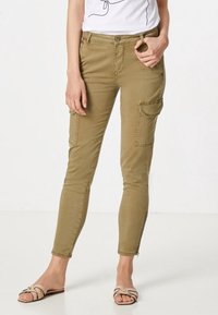 Khaki cargo-housut, joissa on tiukka muotoilu, sivutaskut ja nilkkavetoketjut. Yhdistetty valkoisen graafisen t-paidan ja vaaleiden sandaalien kanssa.