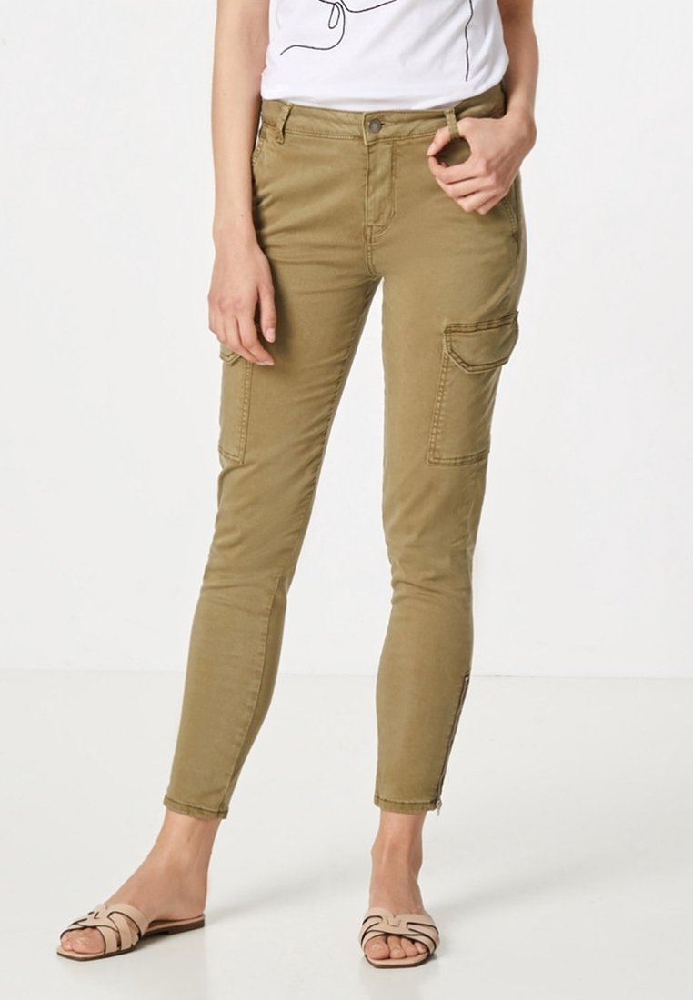 Khaki cargo-housut, joissa on tiukka muotoilu, sivutaskut ja nilkkavetoketjut. Yhdistetty valkoisen graafisen t-paidan ja vaaleiden sandaalien kanssa.