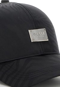 Gorra negra con un patrón texturizado, que presenta una placa de logo de metal plateado, visera curvada y detalles cosidos. Hecha de tela suave.
