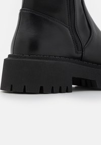 Svart läderankelboot med dragkedja på sidan, tjock gummisula med mönster och rund tå. Slät textur med minimalt med sömmar.