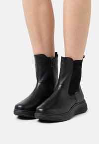Botas de tobillo de cuero negro con paneles laterales elásticos, cierre de cremallera, punta redondeada y suela de goma texturizada. Acabado suave con un detalle mínimo.