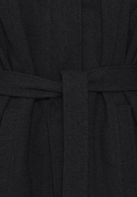 Robe in lana nera con tessuto testurizzato, cintura integrata e tasche laterali. Presenta un design semplice ed elegante con cuciture pulite.