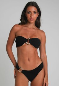 Svart bikini-set med texturerad tyg, ärmlös topp med gyllene detaljer i mitten och matchande underdel med sidodetaljer.