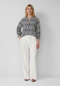 Navybluse mit weißem Blattmuster, gerafften Ärmeln und einer Krawattenhalslinie, kombiniert mit hochgeschnittenen weißen weiten Hosen und flachen Sandalen.