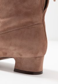 Bruna mockaskinnsankleboots med låg klack och rena sömmar. Materialet har en mjuk textur med en matt yta och en strömlinjeformad silhuett.