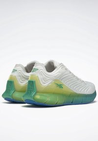 Baskets de sport blanches avec une tige texturée, présentant des accents dégradés verts et bleus sur la semelle et un logo Reebok bien en vue sur le côté.