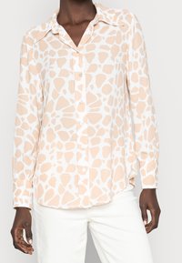 Chemise à manches longues à boutons en pêche clair avec un motif abstrait blanc. Elle possède un col français et un ourlet arrondi. Tissu lisse et léger.