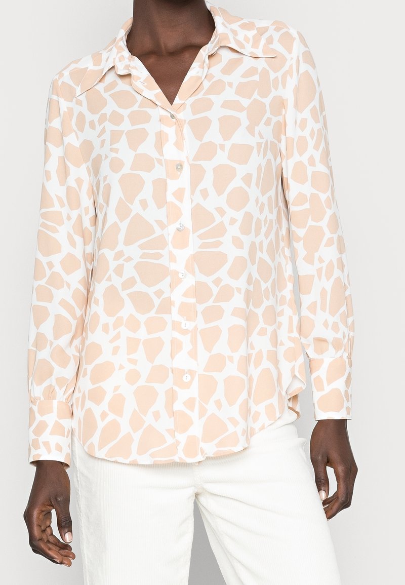 Chemise à manches longues à boutons en pêche clair avec un motif abstrait blanc. Elle possède un col français et un ourlet arrondi. Tissu lisse et léger.