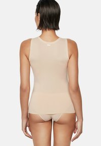Haut sans manches de couleur chair avec un col rond, fabriqué en tissu lisse et extensible. Présente un discret logo au dos.