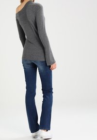 Camisa gris de manga larga con diseño off-shoulder, combinada con jeans azules. Textura suave, silueta ajustada y zapatillas blancas visibles.