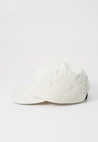 Beige canvas cap with a curved brim, two ventilation eyelets on each side, and a small tag on the side. Simple, unembellished design.