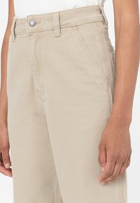 Béžové tvídy kalhoty s fitted pasem, knoflíkovým zapínáním, bočními kapsami a viditelným šitím podél švů.