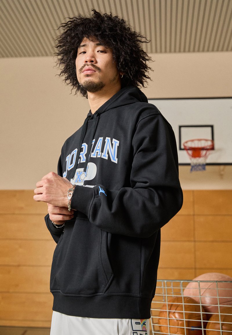 Felpa nera con cappuccio con logo "JORDAN" in blu, tasca a canguro, polsini a costine e un canestro da basket rosso sullo sfondo.