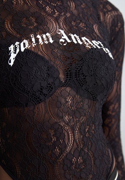 Schwarzer Spitzen-Bodysuit mit floralem Muster, transparentem Material und langen Ärmeln; "Pain Angel"-Schriftzug in Weiß auf der Brust gestickt.