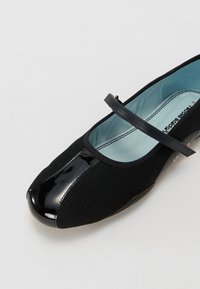 Sabrinas de malha pretas com bico brilhante preto e uma fita fina no tornozelo. Forro interior azul claro. Sola plana com mínimos acabamentos em metal.