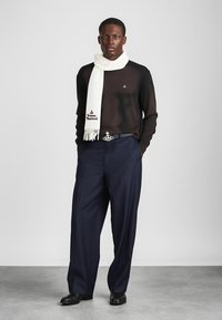 Črna pletena pulover, bela šal z resicami, mornarsko modre hlače z drobnimi črtami, pas s kovinskim okrasjem v obliki kroga, črne čevlje. Preprost, elegantno oblikovan videz.