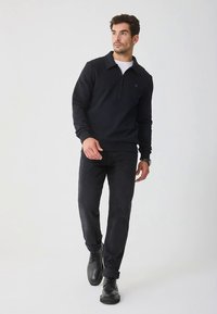 Pullover nero con collo a mezza zip, realizzato in materiale morbido. Abbinato a jeans scuri e scarpe nere, per un look casual.